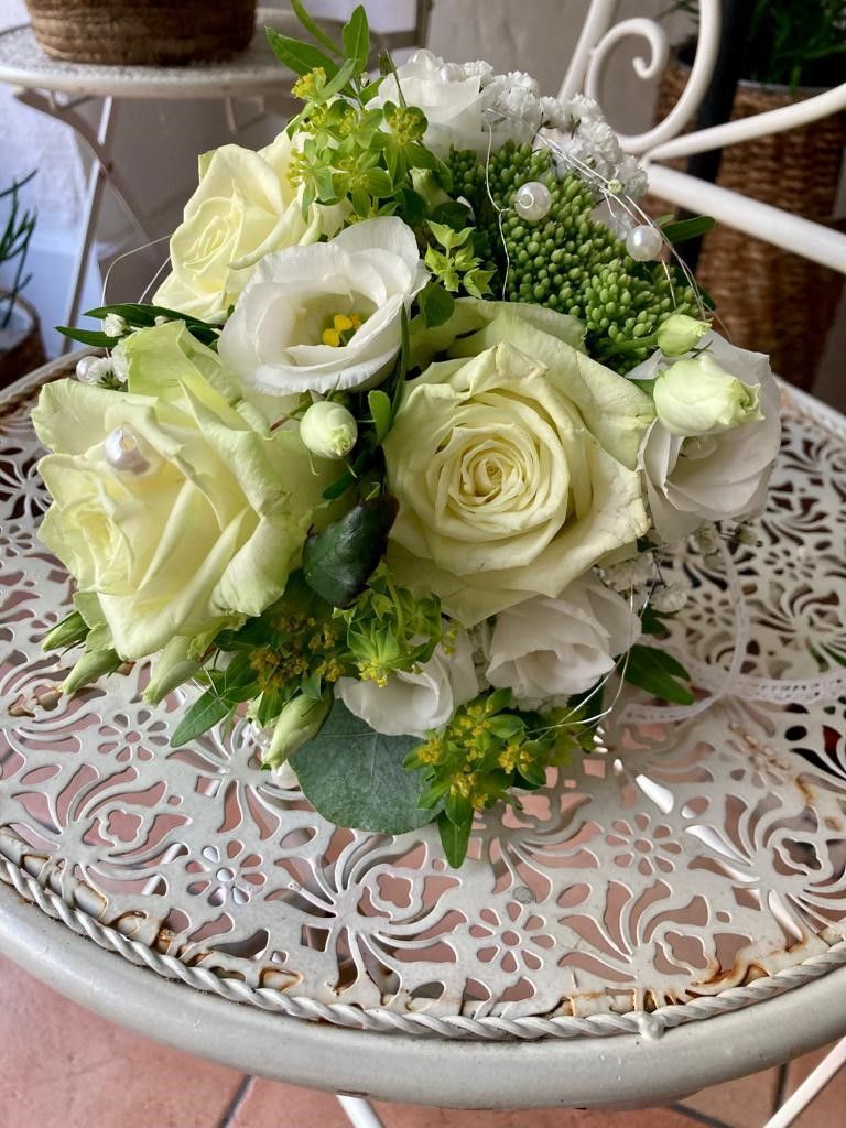 Ein Strauß weißer Rosen und Grünpflanzen steht auf einem weißen Tisch.