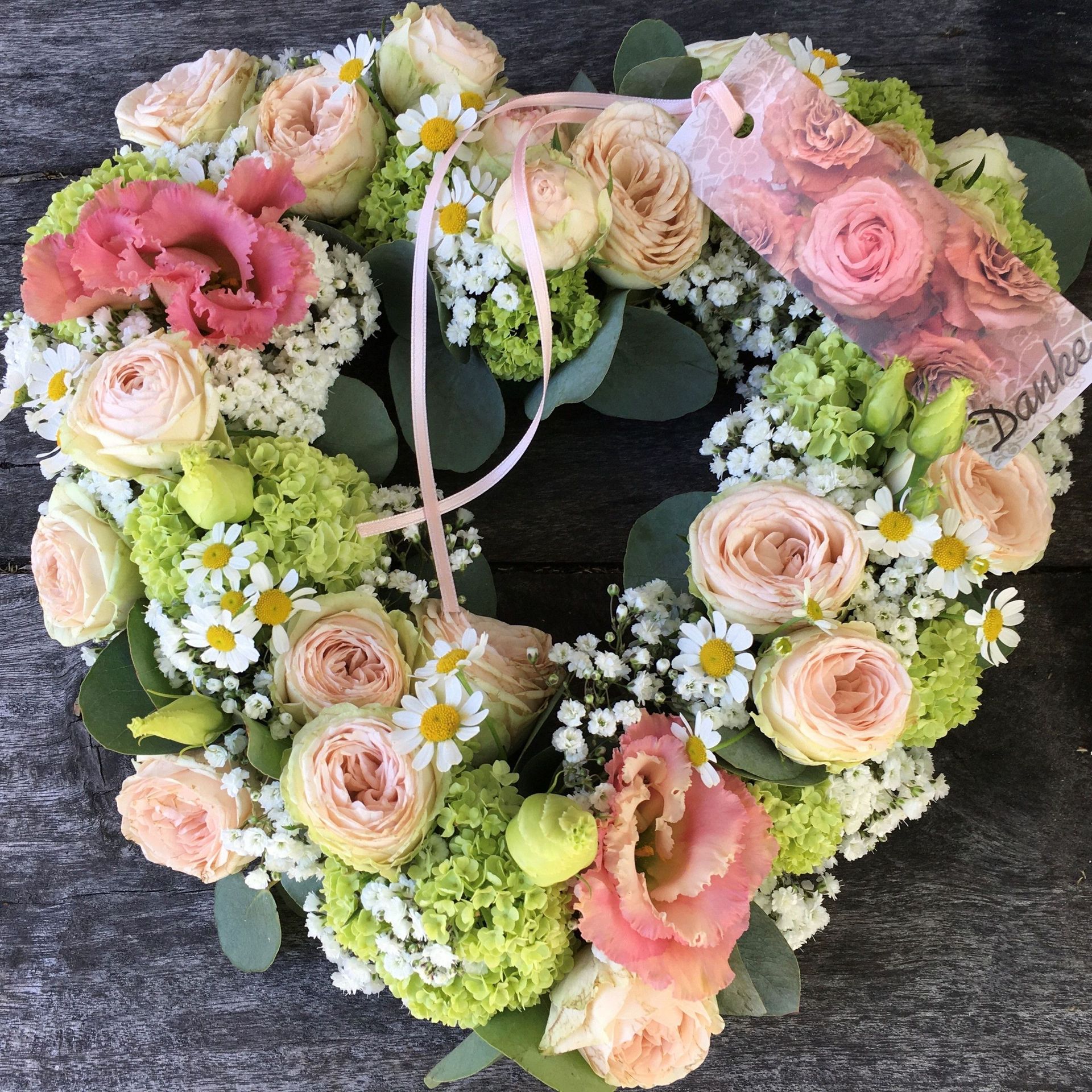 Ein Kranz aus rosa und grünen Blumen auf einem Holztisch