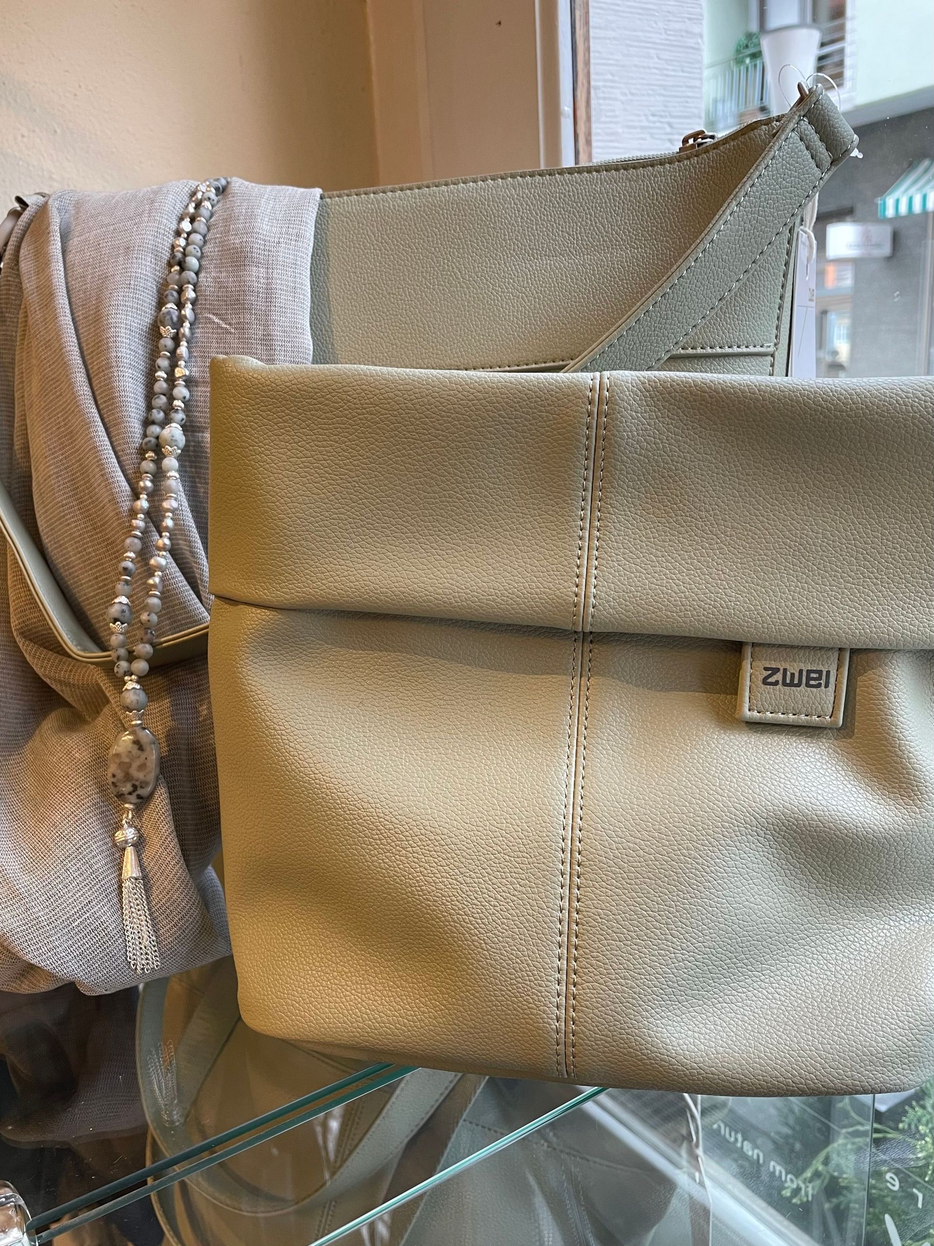 Eine Handtasche liegt neben einem Pullover auf einem Glasregal.