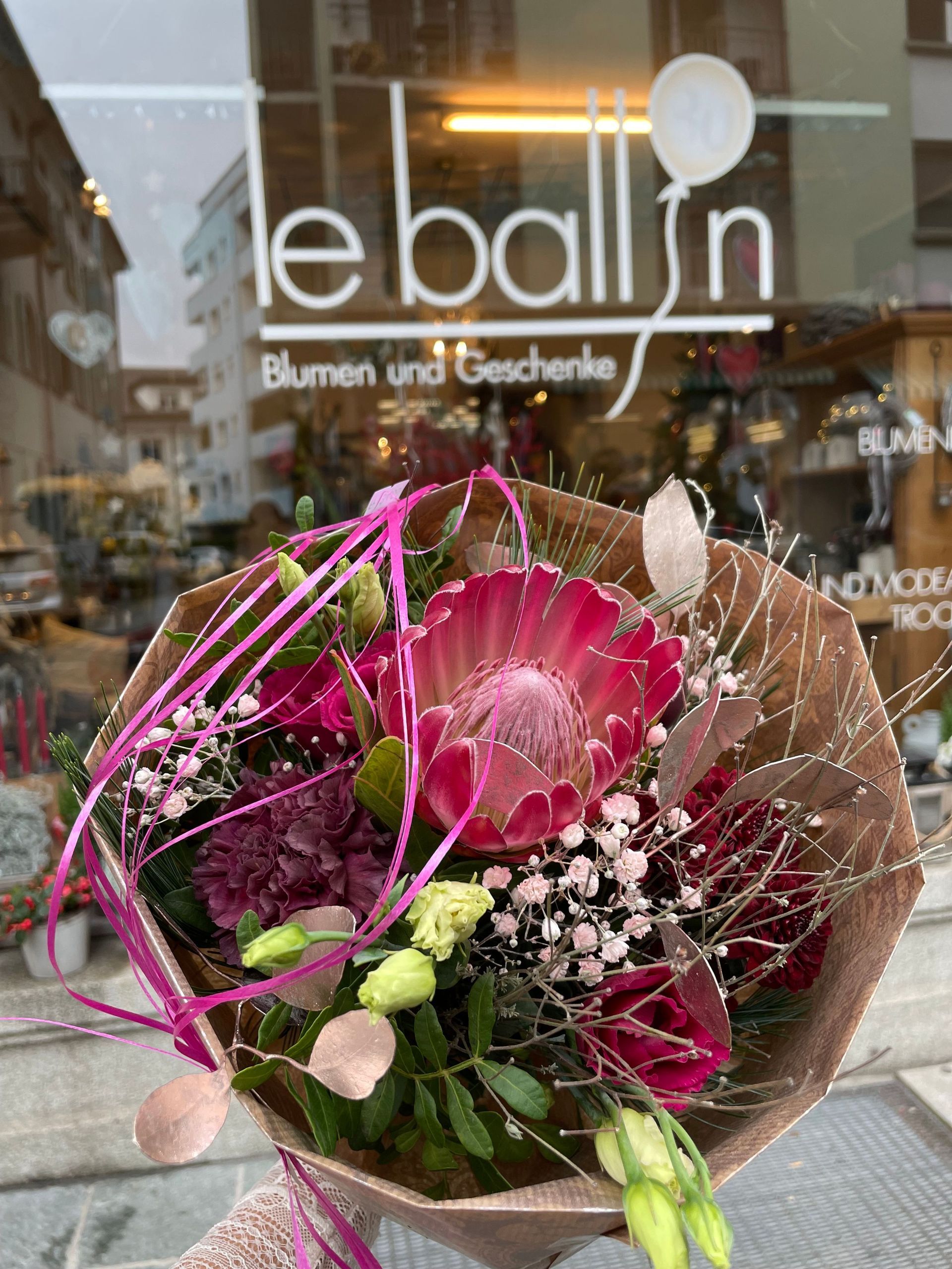 Eine Person hält einen Blumenstrauß vor einem Schaufenster.