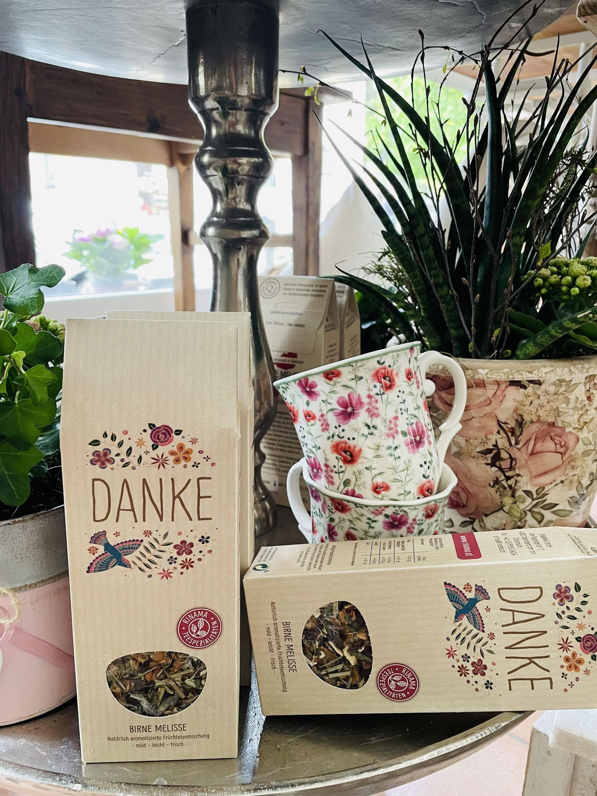 Eine Schachtel Danke-Tee steht neben einer Tasse und Untertasse auf einem Tisch.