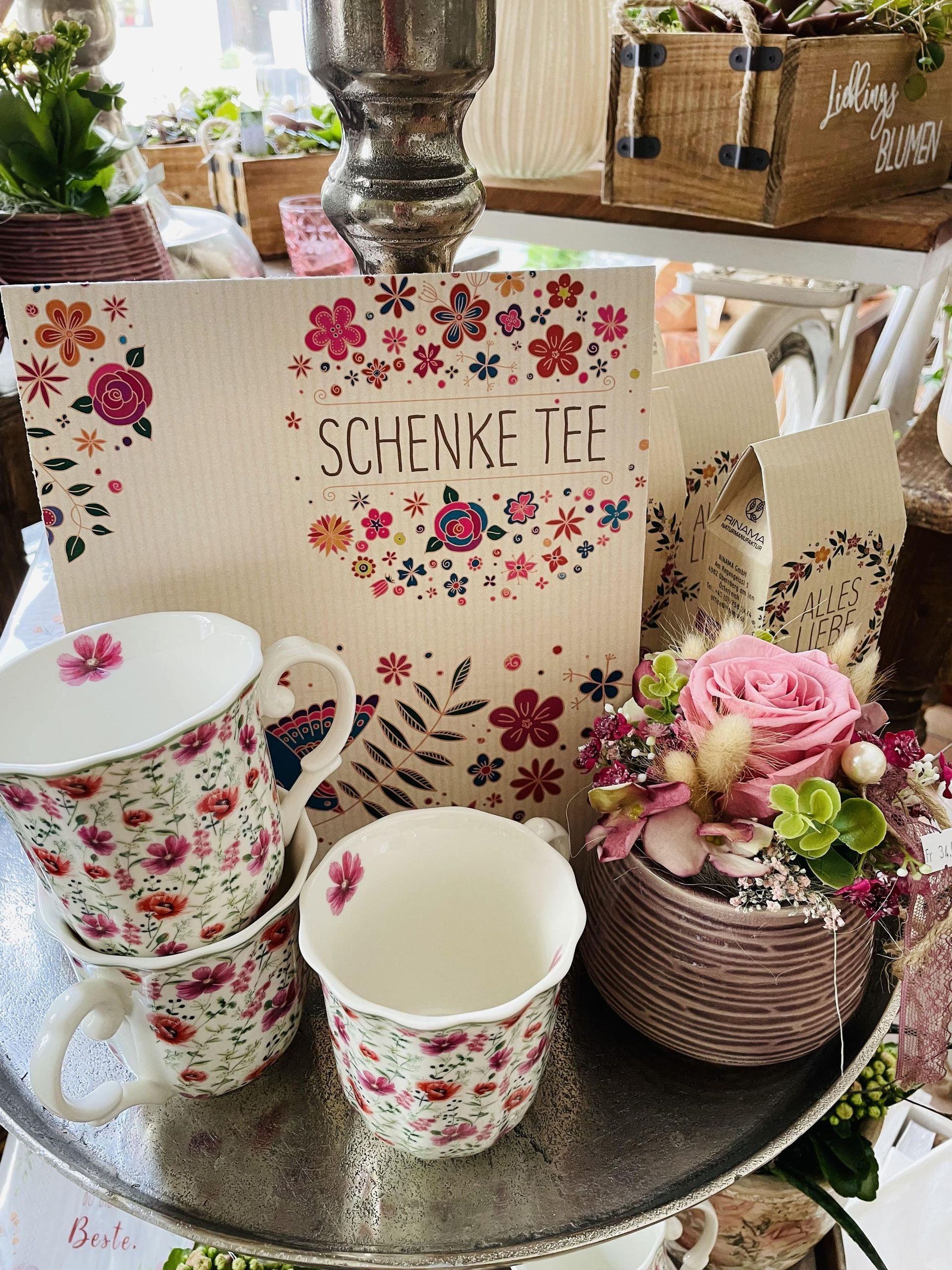 Ein Tablett mit Blumen und Tassen darauf und einem Schild mit der Aufschrift „Schenke te“.