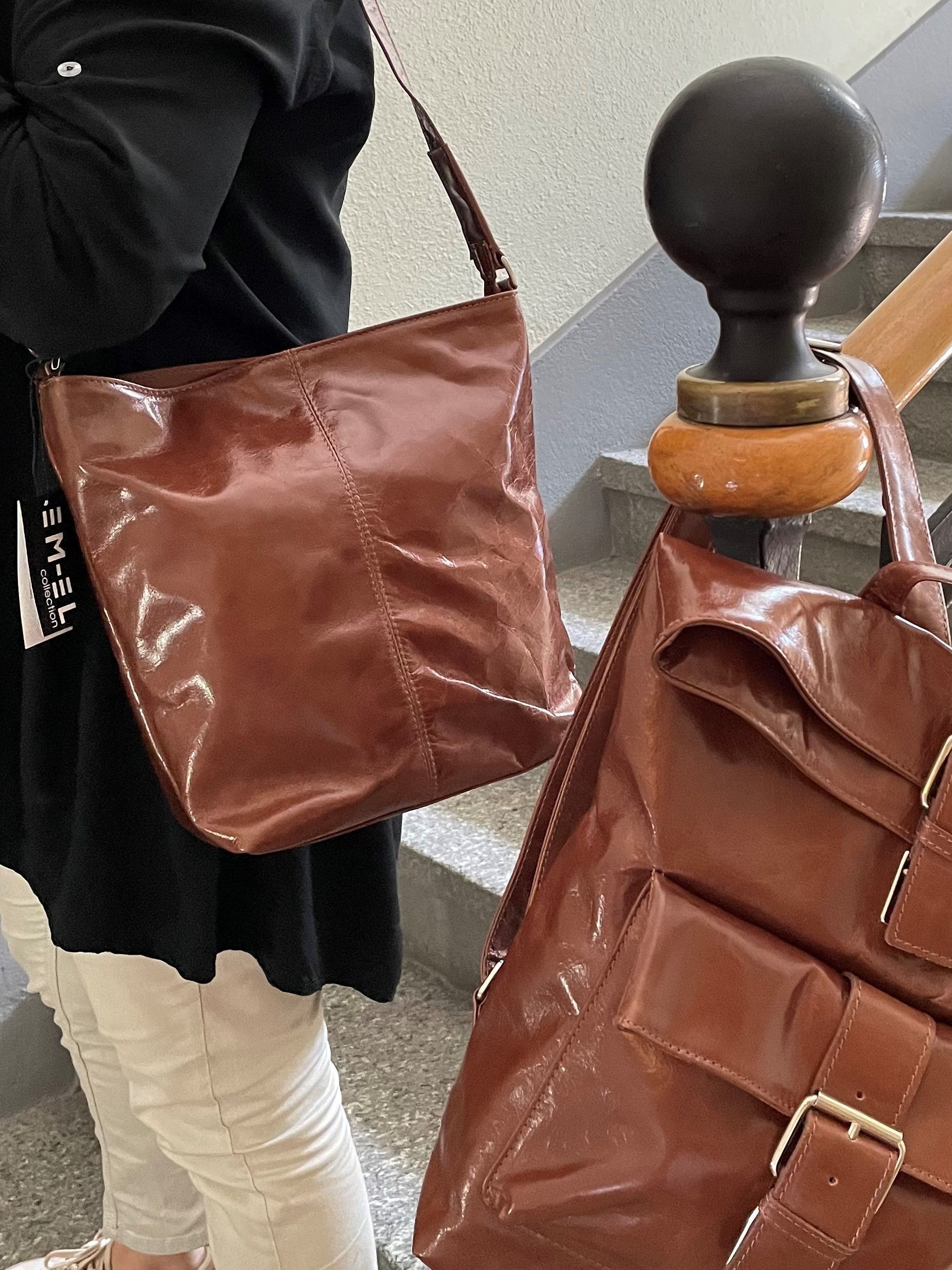 Eine Frau hält eine braune Lederhandtasche und einen braunen Lederrucksack.