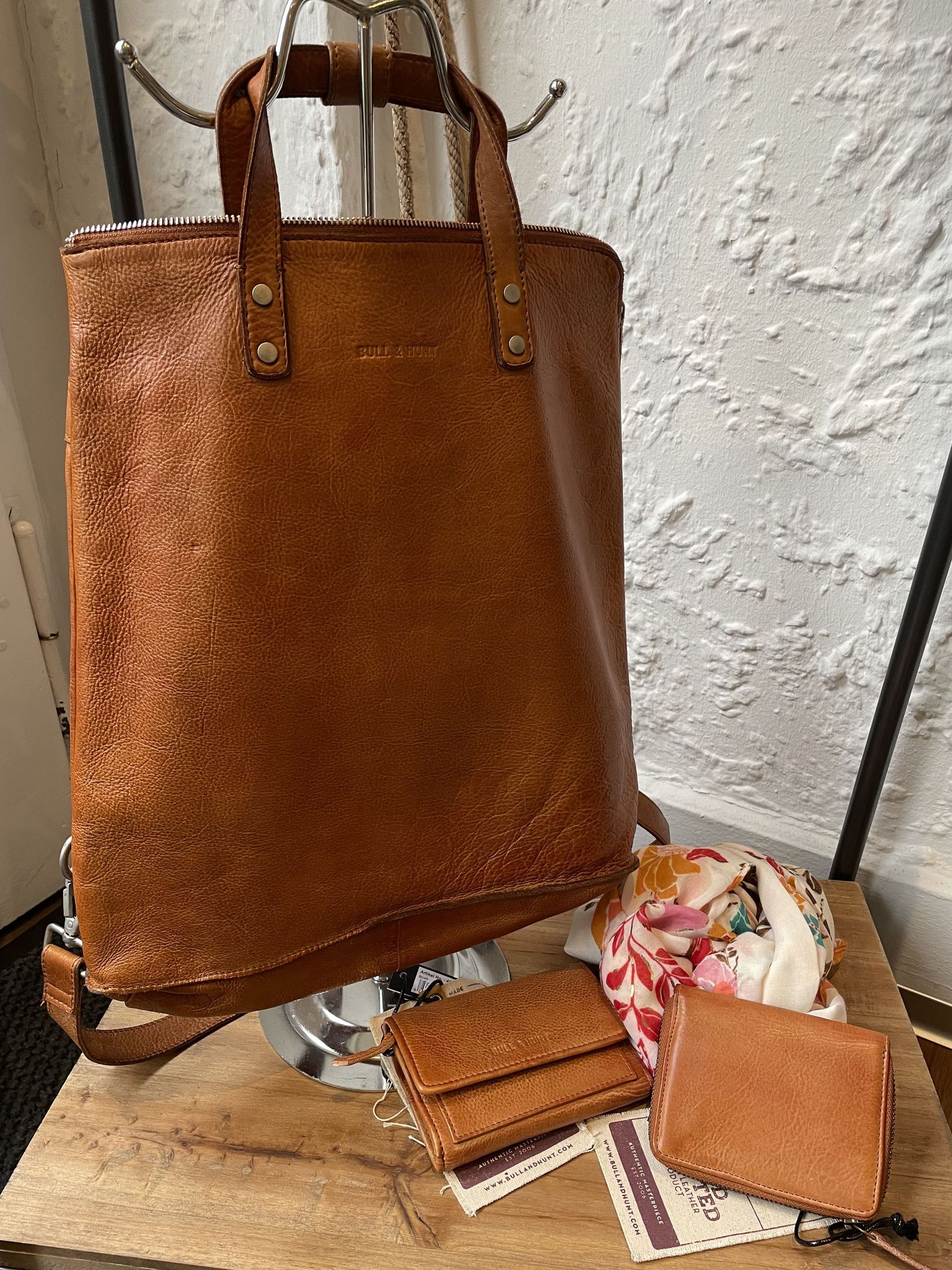 Auf einem Holztisch liegt eine braune Einkaufstasche aus Leder.