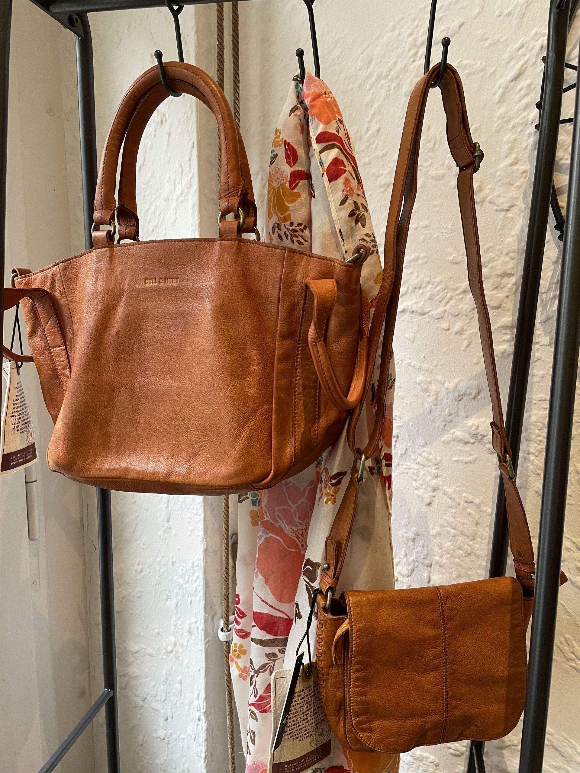 Zwei braune Lederhandtaschen hängen an einem Gestell