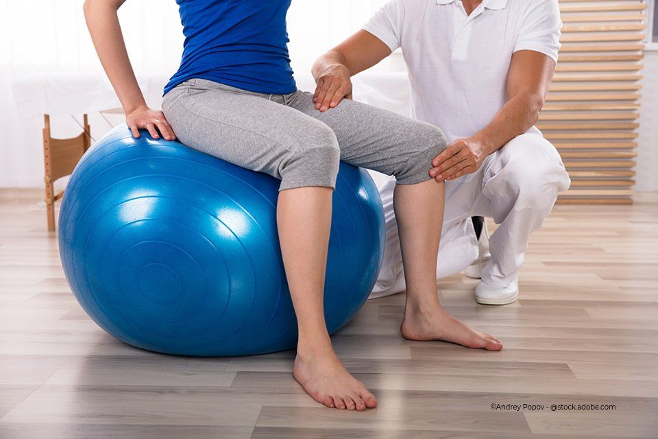 Frau sitzt auf Gymnastikball, während Mitarbeiter der Körpermanufaktur ihre Beine hält