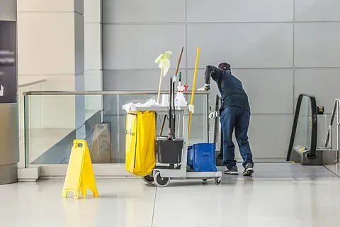 Un hombre está limpiando el piso de un edificio con un trapeador.