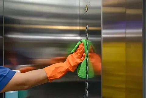 Una persona está limpiando un ascensor de acero inoxidable con un paño.