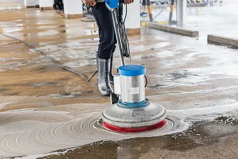 Una persona está limpiando un piso de concreto con una máquina.