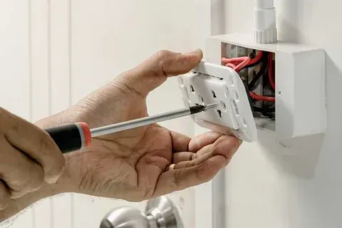 Una persona está arreglando un tomacorriente eléctrico con un destornillador.