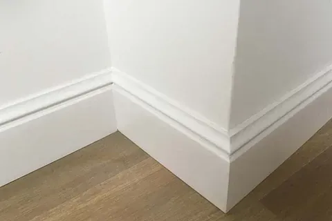 Un primer plano de un rodapié blanco sobre un suelo de madera.