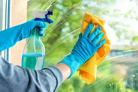 Una persona está limpiando una ventana con una botella de spray y un paño.