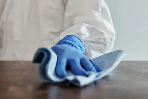 Una persona que lleva guantes azules está limpiando una mesa de madera con un paño.