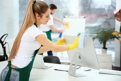 Una mujer está limpiando un monitor de computadora en una oficina.