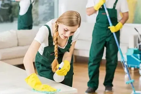 Una mujer está limpiando una mesa con una botella de spray en una sala de estar.