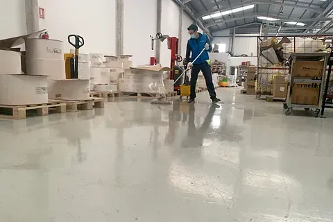 Un hombre está limpiando el suelo de un almacén con un trapeador.