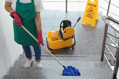 Una mujer está limpiando las escaleras con un trapeador y un balde.