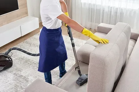 Un hombre está limpiando un sofá con una aspiradora.