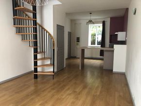 Salon moderne vide avec parquet, escalier en colimaçon et coin cuisine.