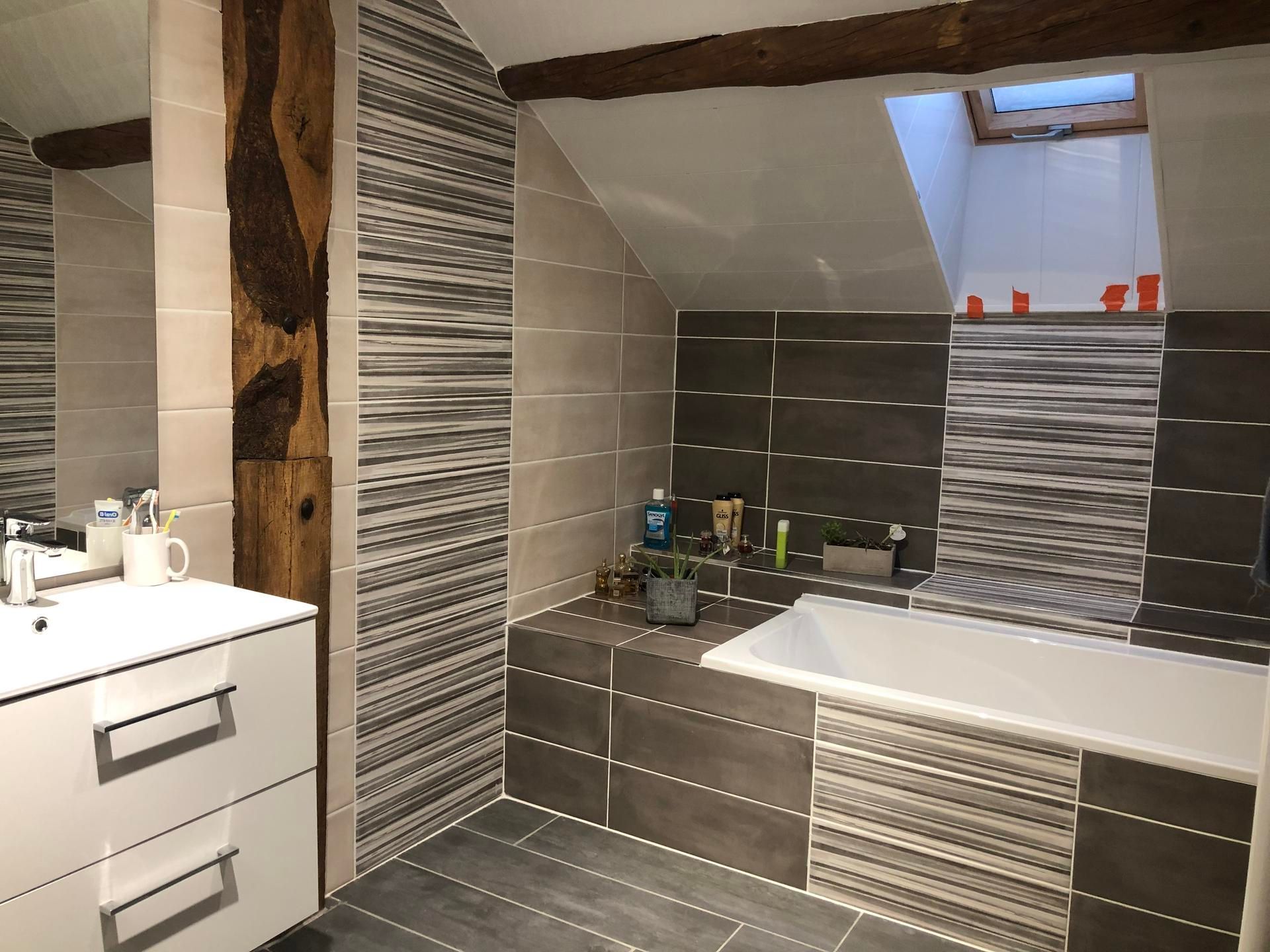 Salle de bains moderne avec murs carrelés, baignoire blanche et meuble vasque sous un puits de lumière.