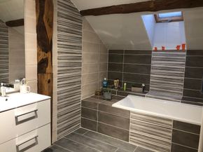 Salle de bains moderne avec murs carrelés, baignoire blanche et meuble vasque sous un puits de lumière.