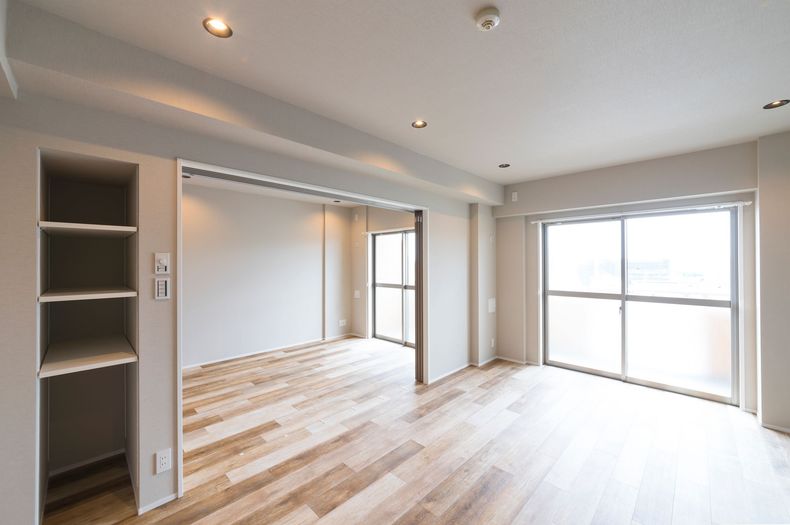Pièce moderne, lumineuse et vide, avec parquet clair, spots encastrés et grandes fenêtres.