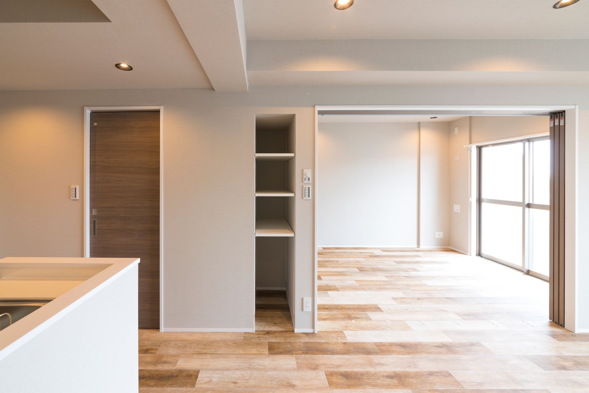 Intérieur d'un appartement moderne vide avec un espace de vie ouvert, un comptoir de cuisine et une baie vitrée menant au balcon.