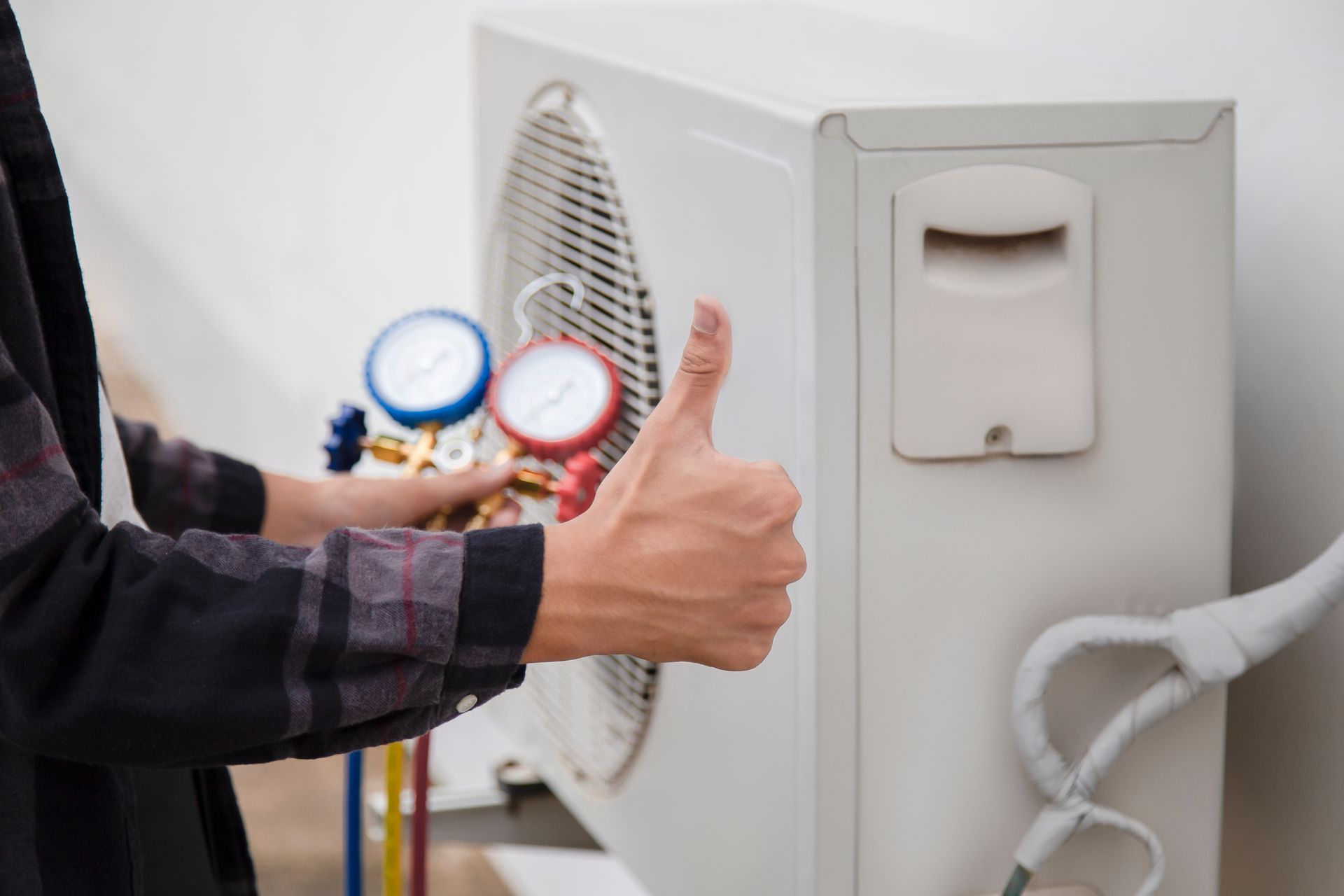 Une personne fait un signe de pouce levé à côté d'une unité extérieure de climatisation.
