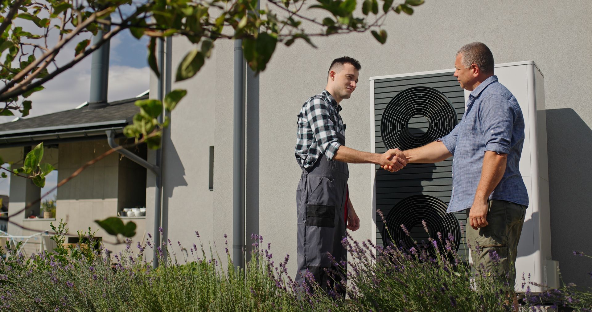 Un technicien qui serre la main de son client devant une unité extérieure de pompe à chaleur.