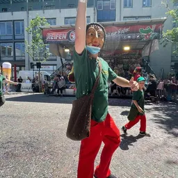 Ein Mann mit einer Maske steht bei einer Parade auf Stelzen.