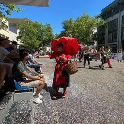 Eine Frau in einem roten Kleid hält einen roten Regenschirm und einen Korb.