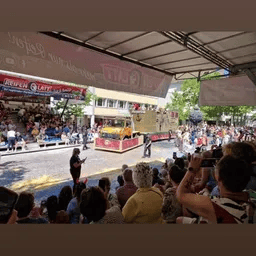Eine Menschenmenge schaut sich eine Parade an , während ein Lastwagen die Straße entlang fährt.