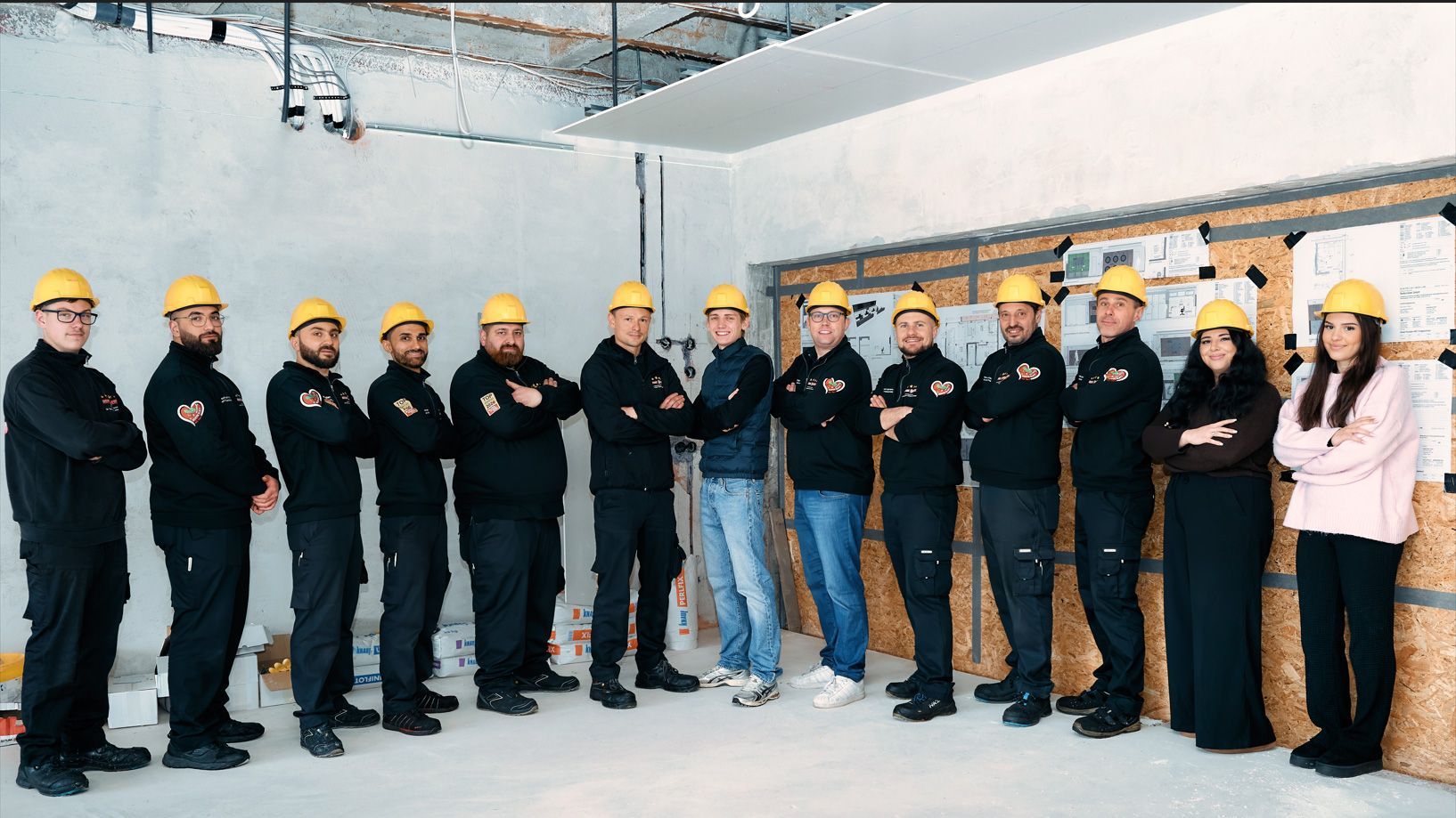 Eine Gruppe von Bauarbeitern mit Schutzhelmen posiert in einem noch unfertigen Gebäude