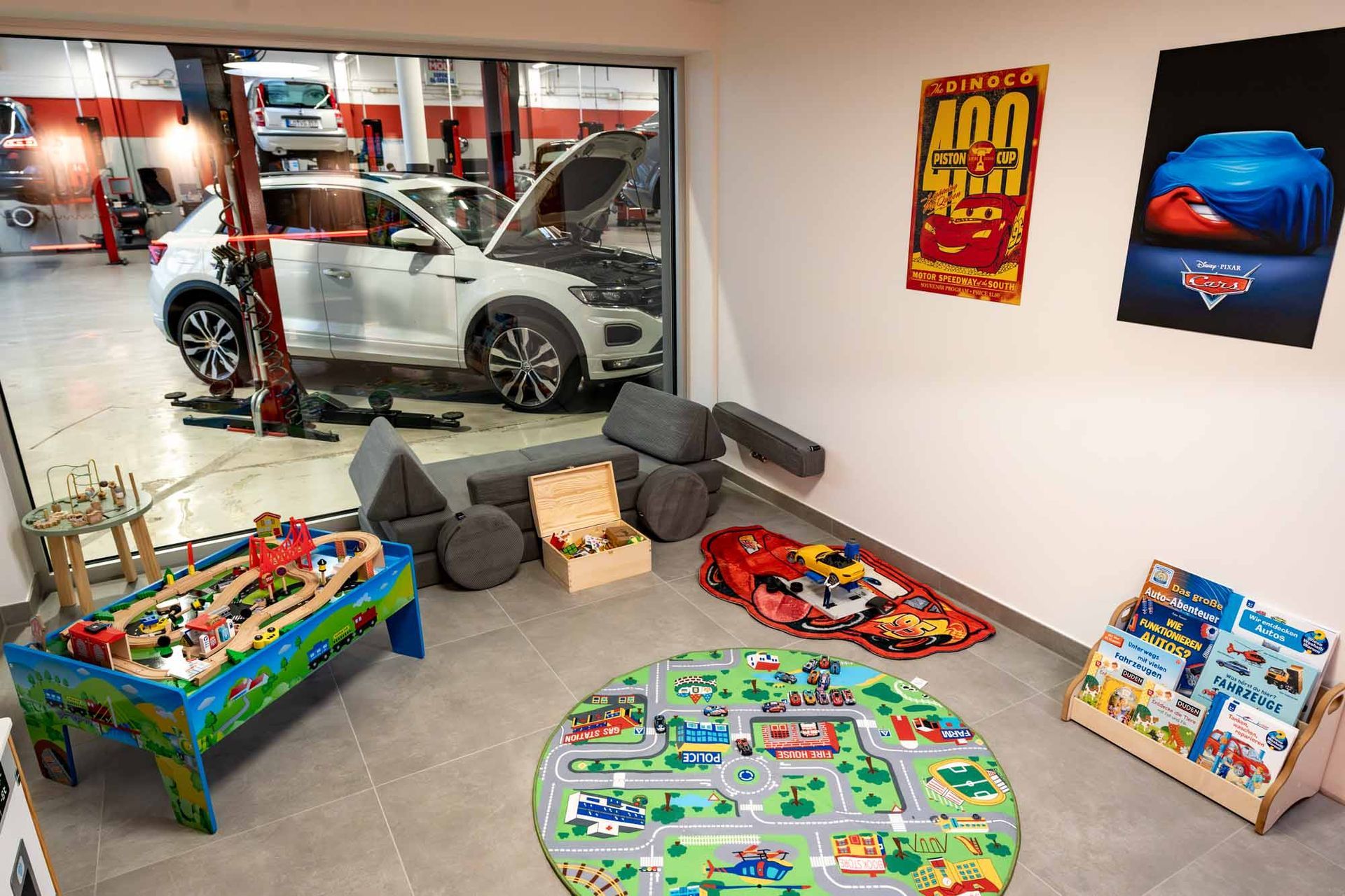 Kids’ playroom with toy table, play mat, storage bins, and wall art beside a garage window