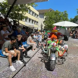 Eine Gruppe von Menschen sitzt auf einer Tribüne und sieht sich eine Parade an.