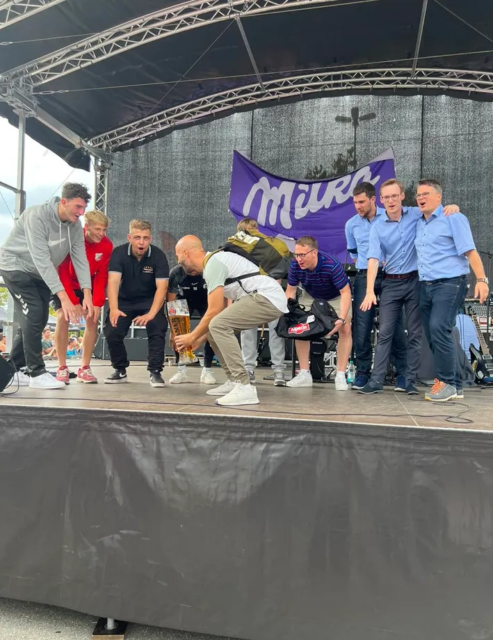Eine Gruppe Männer steht auf einer Bühne vor einem Milka-Banner.