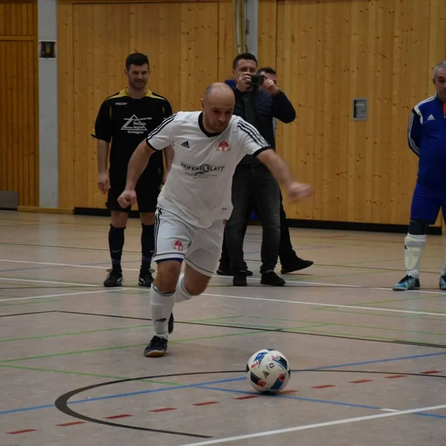 Ein Mann in einem weißen Adidas-Shirt kickt einen Fußball