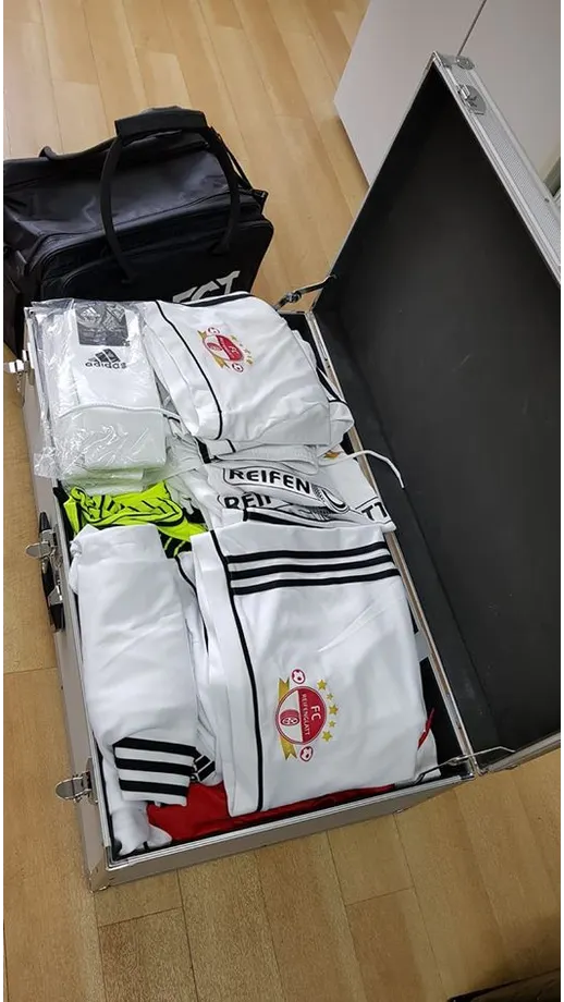 Auf einem Holzboden steht ein Koffer voller Kleidung.