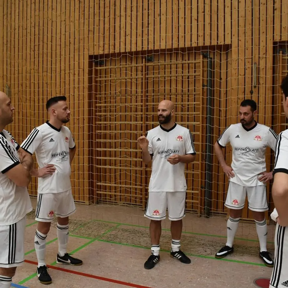 Eine Gruppe von Fußballspielern steht in einer Turnhalle und unterhält sich miteinander.