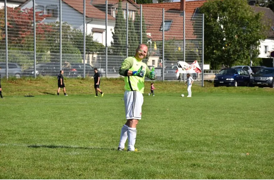Ein Mann in einem grünen Trikot steht auf einem Fußballfeld und hält einen Fußball.