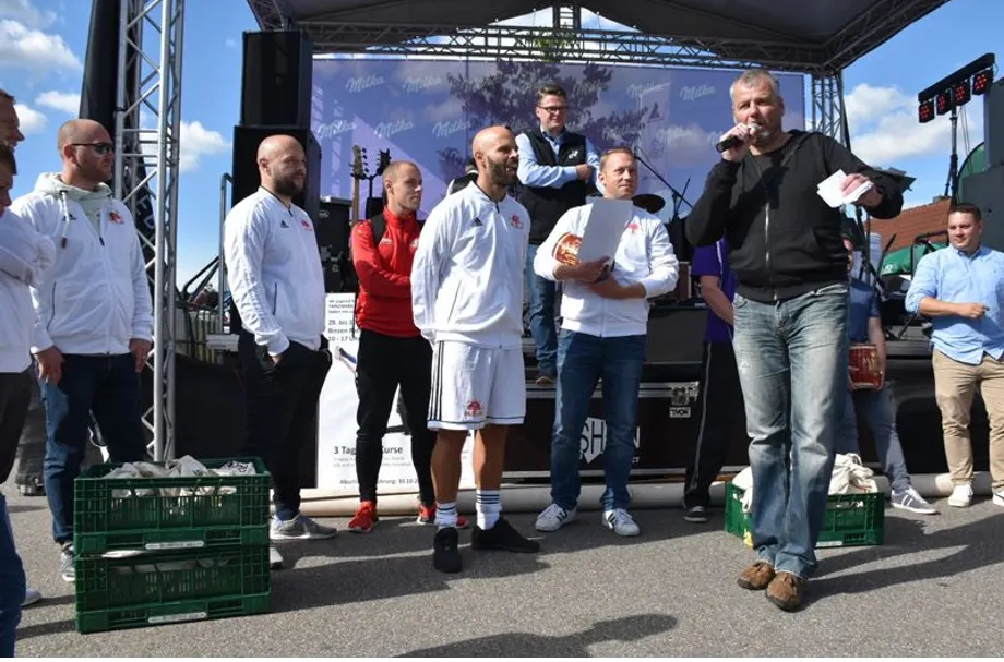 Eine Gruppe von Männern steht vor einer Bühne und ein Mann hält ein Mikrofon