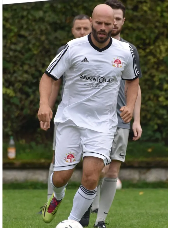 Ein Mann mit Bart spielt auf einem Feld Fußball.