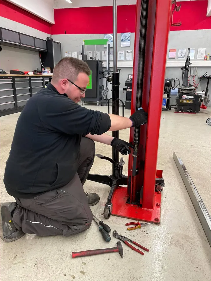 Ein Mann kniet und arbeitet an einer Hebebühne in einer Garage.