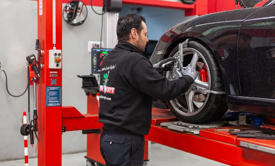 Ein Mann arbeitet auf einer Hebebühne in einer Garage an einem Auto.