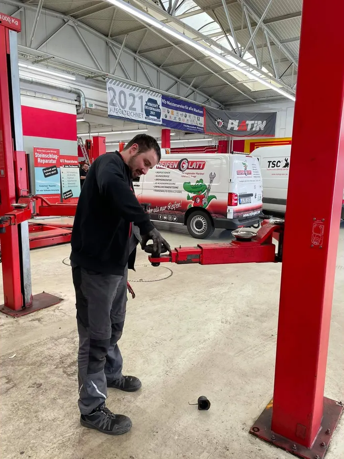 Ein Mann arbeitet auf einer Hebebühne in einer Garage an einem Auto.