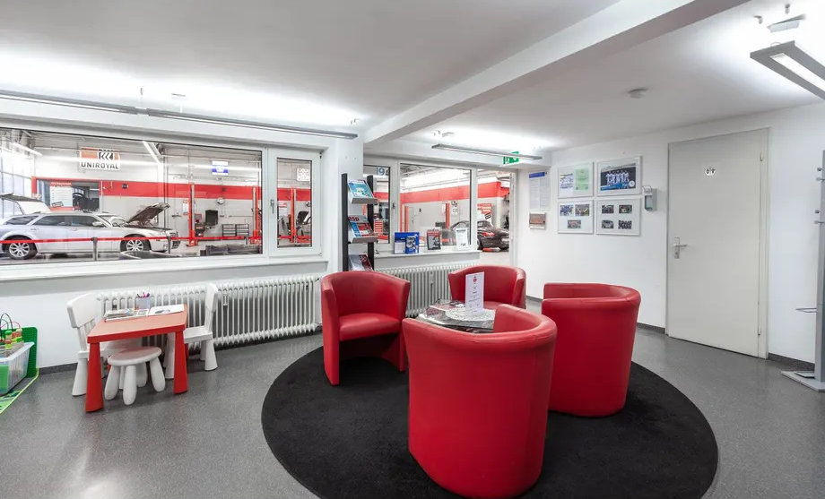 Ein Wartezimmer mit roten Stühlen und einem Tisch