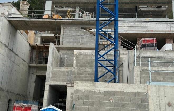Un edificio en construcción con una grúa azul delante.
