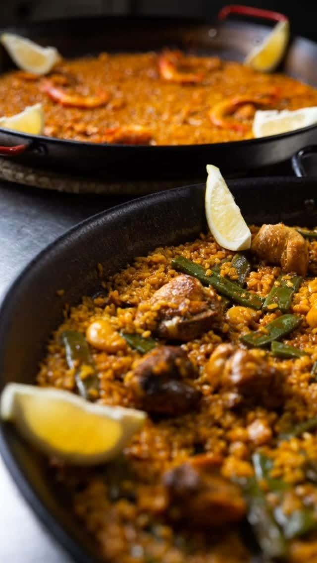 Dos sartenes de paella con rodajas de limón sobre una mesa.
