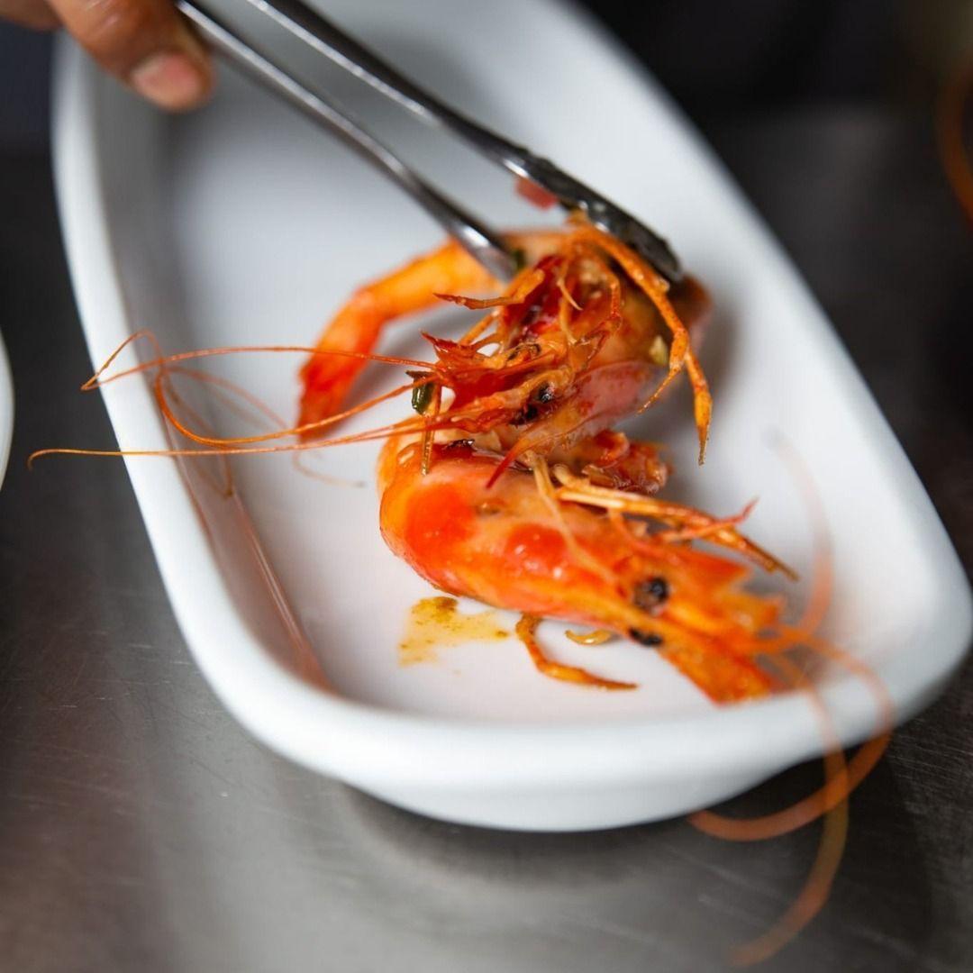 Una persona sostiene pinzas sobre un plato de camarones.