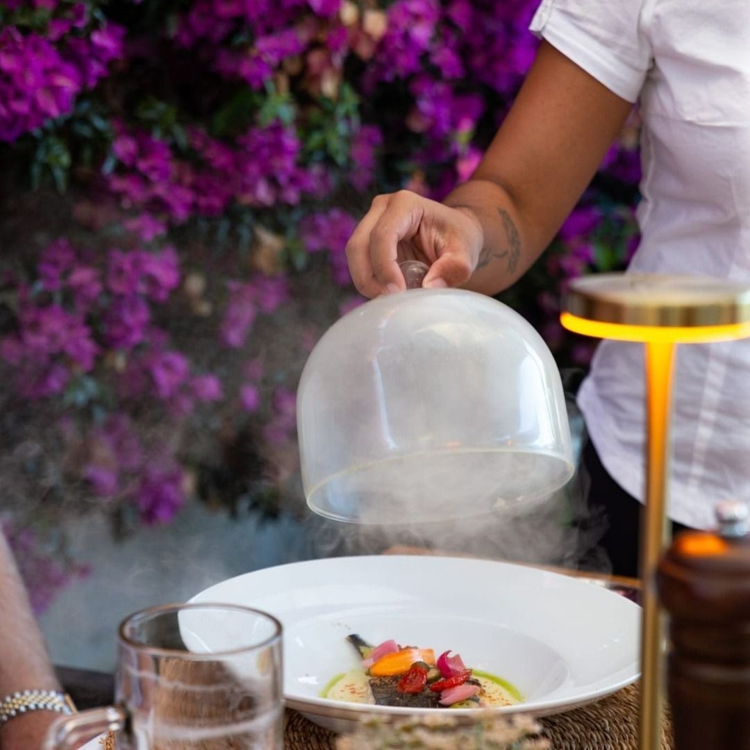 Una mujer sostiene una cúpula sobre un plato de comida.